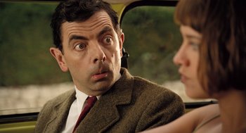 Movie still from “Mr. Bean's Holiday” (2007), directed by Steve Bendelack – A person sitting in a car with another person; Close Up shot, Over the shoulder angle