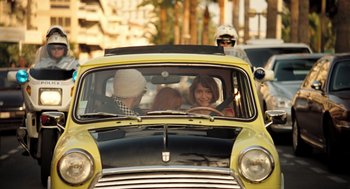 Movie still from “Mr. Bean's Holiday” (2007), directed by Steve Bendelack – A group of people riding in the back of a yellow car; Wide shot, High angle