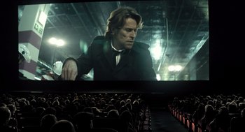 Movie still from “Mr. Bean's Holiday” (2007), directed by Steve Bendelack – A man in a black suit is on a large screen; Wide shot, Low angle