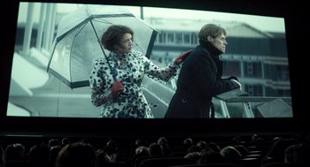 Movie still from “Mr. Bean's Holiday” (2007), directed by Steve Bendelack – Two women are standing under an umbrella in front of a movie screen; Medium shot, Low angle