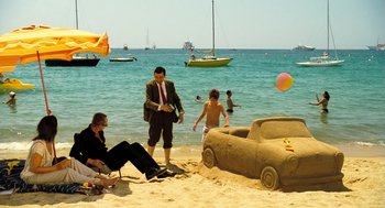 Movie still from “Mr. Bean's Holiday” (2007), directed by Steve Bendelack – Two men and a woman on the beach near a sand car; Wide shot, High angle
