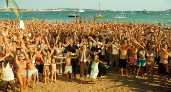 Movie still from “Mr. Bean's Holiday” (2007), directed by Steve Bendelack – A crowd of people standing on a beach with their hands up; Extreme Wide shot, High angle