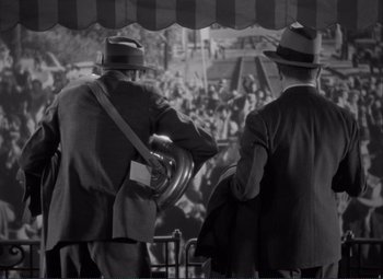 Movie still from “Mr. Deeds Goes to Town” (1936), directed by Frank Capra – A couple of men in suits and hats are standing in front of an audience; Medium shot, High angle