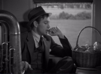 Movie still from “Mr. Deeds Goes to Town” (1936), directed by Frank Capra – A black and white photo of a man sitting on a train; Medium shot, Over the shoulder angle