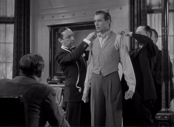 Movie still from “Mr. Deeds Goes to Town” (1936), directed by Frank Capra – A group of men standing next to each other in front of a fireplace; Medium shot, Over the shoulder angle