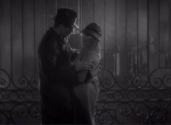 Movie still from “Mr. Deeds Goes to Town” (1936), directed by Frank Capra – A man and a woman standing next to each other in front of an iron gate; Medium shot, High angle