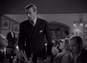 Movie still from “Mr. Deeds Goes to Town” (1936), directed by Frank Capra – A man standing in front of a group of people at a table; Medium shot, Low angle