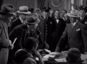 Movie still from “Mr. Deeds Goes to Town” (1936), directed by Frank Capra – A black and white photo of a group of men in suits and hats; Medium shot, Over the shoulder angle