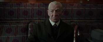 Movie still from “Mr. Holmes” (2015), directed by Bill Condon – An older man in a suit and tie sitting on a couch; Close Up shot, Over the shoulder angle