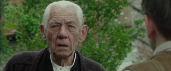Movie still from “Mr. Holmes” (2015), directed by Bill Condon – An old man with white hair is looking at the camera; Close Up shot, Over the shoulder angle