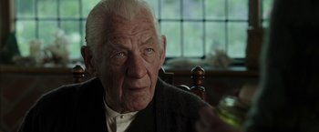 Movie still from “Mr. Holmes” (2015), directed by Bill Condon – An old man sitting at a table with a glass in his hand; Close Up shot, Over the shoulder angle