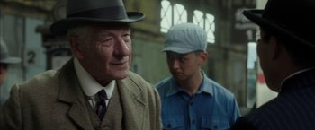 Movie still from “Mr. Holmes” (2015), directed by Bill Condon – A man wearing a hat standing next to another man wearing a hat; Close Up shot, Over the shoulder angle
