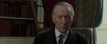 Movie still from “Mr. Holmes” (2015), directed by Bill Condon – An older man in a suit and tie sitting in a chair; Close Up shot, Low angle