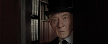 Movie still from “Mr. Holmes” (2015), directed by Bill Condon – An old man wearing a black hat and a suit; Close Up shot, Over the shoulder angle