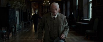 Movie still from “Mr. Holmes” (2015), directed by Bill Condon – An older man in a suit and tie walking in a hallway; Medium shot, Low angle