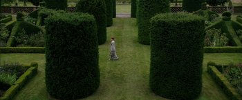 Movie still from “Mr. Holmes” (2015), directed by Bill Condon – A person walking through a garden with hedges around them; Extreme Wide shot, High angle