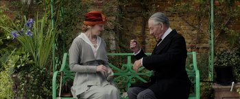 Movie still from “Mr. Holmes” (2015), directed by Bill Condon – An older man and woman sitting on top of a green bench; Medium shot, Over the shoulder angle