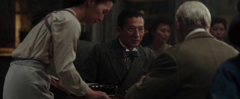 Movie still from “Mr. Holmes” (2015), directed by Bill Condon – A man in a suit and tie is sitting at a table; Medium shot, Over the shoulder angle