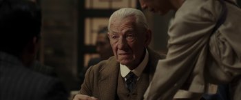 Movie still from “Mr. Holmes” (2015), directed by Bill Condon – An old man in a suit and tie looking at the camera; Close Up shot, Over the shoulder angle