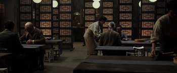 Movie still from “Mr. Holmes” (2015), directed by Bill Condon – A person standing at a table with a person sitting at a table; Medium shot, Over the shoulder angle