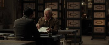 Movie still from “Mr. Holmes” (2015), directed by Bill Condon – An older man sitting at a table with a book; Medium shot, Over the shoulder angle