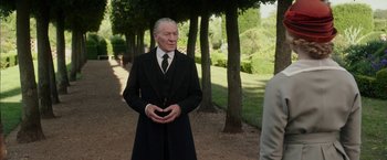 Movie still from “Mr. Holmes” (2015), directed by Bill Condon – An older man in a suit and tie standing in a park; Medium shot, Over the shoulder angle