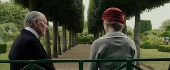 Movie still from “Mr. Holmes” (2015), directed by Bill Condon – A woman with a red hat sitting on top of a bench; Medium shot, Over the shoulder angle