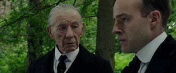 Movie still from “Mr. Holmes” (2015), directed by Bill Condon – A man in a suit and tie standing next to another man in a suit and tie; Close Up shot, Over the shoulder angle