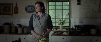Movie still from “Mr. Holmes” (2015), directed by Bill Condon – A woman standing in a kitchen holding a basket of vegetables; Medium shot, Over the shoulder angle