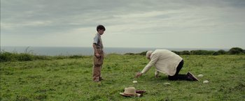 Movie still from “Mr. Holmes” (2015), directed by Bill Condon – Two people in a field looking at a hat on the ground; Wide shot, High angle