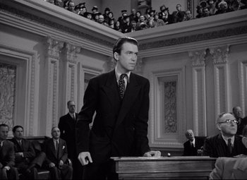 Movie still from “Mr. Smith Goes to Washington” (1939), directed by Frank Capra – A black and white photo of a man in a suit and tie standing in front of a podium; Medium shot, Low angle