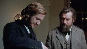 Movie still from “Mrs. Brown” (1997), directed by John Madden – Two men standing next to each other in front of a wall; Medium shot, Over the shoulder angle