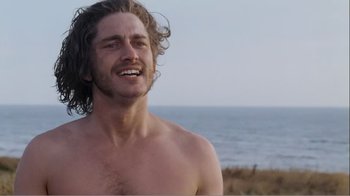 Movie still from “Mrs. Brown” (1997), directed by John Madden – A man with long curly hair and a bare chest is standing on the beach; Close Up shot, Low angle