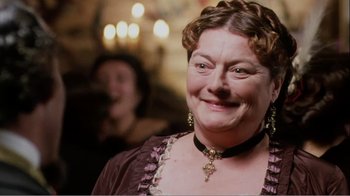 An older woman wearing a purple dress and a cross necklace