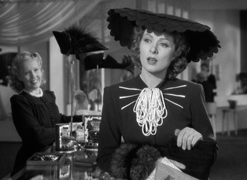 Movie still from “Mrs. Miniver” (1942), directed by William Wyler – A woman in a black dress with a hat on; Medium shot, Over the shoulder angle