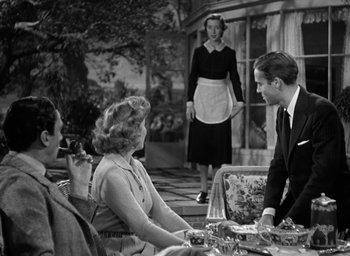 Movie still from “Mrs. Miniver” (1942), directed by William Wyler – An old photo of three people sitting at a dinner table; Medium shot, Over the shoulder angle