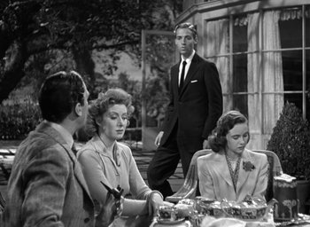 Movie still from “Mrs. Miniver” (1942), directed by William Wyler – A man in a suit standing in front of two women; Medium shot, Low angle