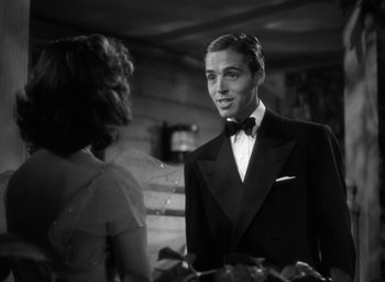 Movie still from “Mrs. Miniver” (1942), directed by William Wyler – A black and white photo of a man in a tuxedo and a woman; Medium shot, Over the shoulder angle