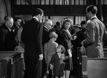Movie still from “Mrs. Miniver” (1942), directed by William Wyler – A group of people standing around each other in a room; Medium shot, Over the shoulder angle