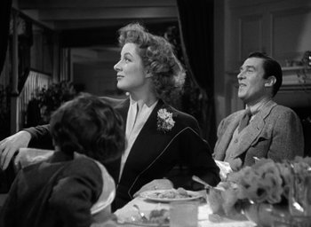 Movie still from “Mrs. Miniver” (1942), directed by William Wyler – An older woman sitting at a table with a man and a child; Medium shot, Over the shoulder angle