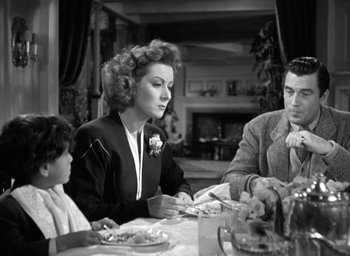 Movie still from “Mrs. Miniver” (1942), directed by William Wyler – A woman sitting at a table with a man and a child; Medium shot, Over the shoulder angle