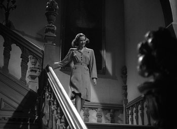 Movie still from “Mrs. Miniver” (1942), directed by William Wyler – A black and white photo of a woman walking down a staircase; Medium shot, Low angle