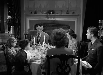 Movie still from “Mrs. Miniver” (1942), directed by William Wyler – A family sitting at a dinner table in front of a fireplace; Wide shot, High angle
