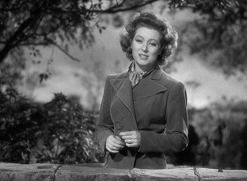 Movie still from “Mrs. Miniver” (1942), directed by William Wyler – An old black and white photo of a woman standing by a stone wall; Close Up shot, Low angle