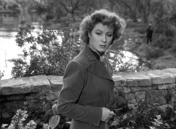 Movie still from “Mrs. Miniver” (1942), directed by William Wyler – An old black and white photo of a woman standing in front of a stone wall; Medium shot, Over the shoulder angle