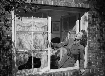 Movie still from “Mrs. Miniver” (1942), directed by William Wyler – A black and white photo of a woman looking out of a window; Medium shot, Low angle