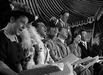 Movie still from “Mrs. Miniver” (1942), directed by William Wyler – A group of men and women singing together; Medium shot, Low angle