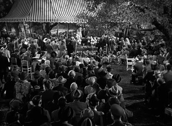Movie still from “Mrs. Miniver” (1942), directed by William Wyler – A crowd of people sitting under a striped tent; Extreme Wide shot, High angle