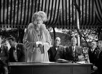 Movie still from “Mrs. Miniver” (1942), directed by William Wyler – An older woman wearing a fur coat holding a piece of paper in her hand; Medium shot, Low angle