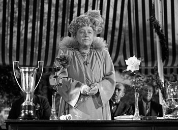 Movie still from “Mrs. Miniver” (1942), directed by William Wyler – An older woman dressed as a lady holding a rose; Medium shot, Low angle